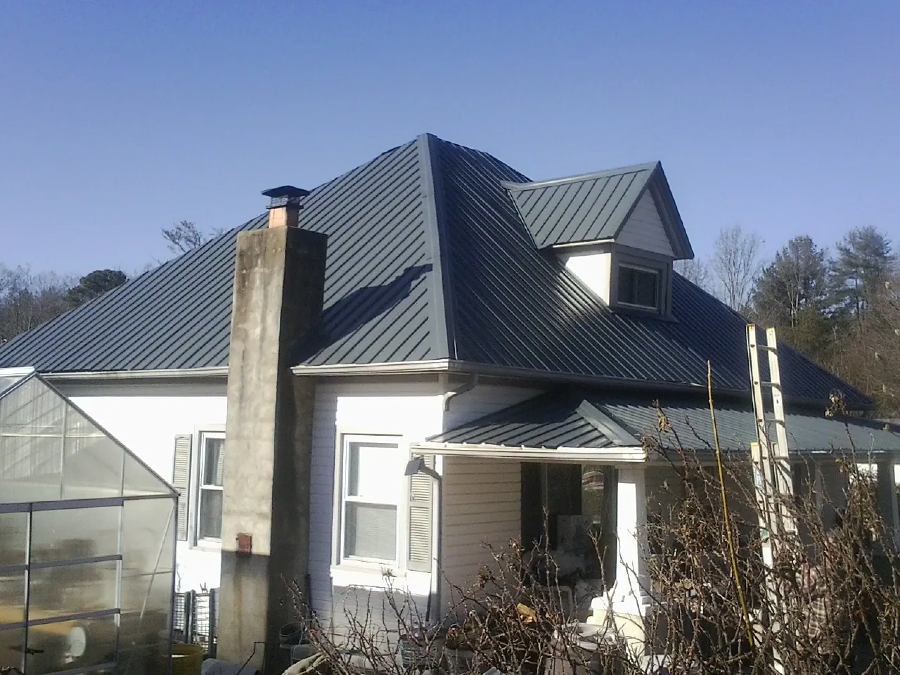 Dark blue standing seam metal roof on a white farmhouse with dormer — Slate & Tile Roof Repair by Roofing Brothers in Carmine