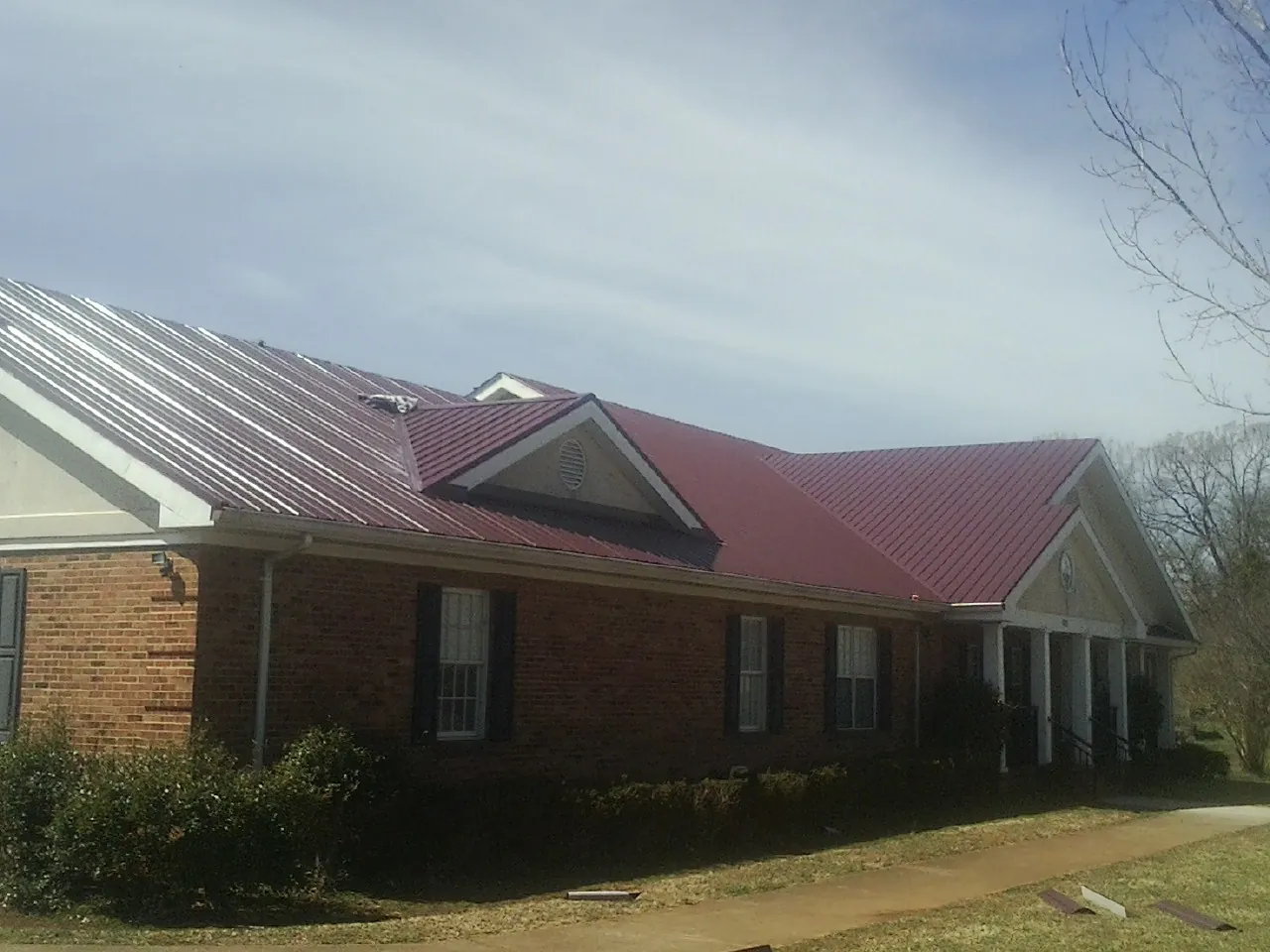 Red metal roof with gabled entries on a long brick building, from a Hail Damage Roof Repair job in Carmine