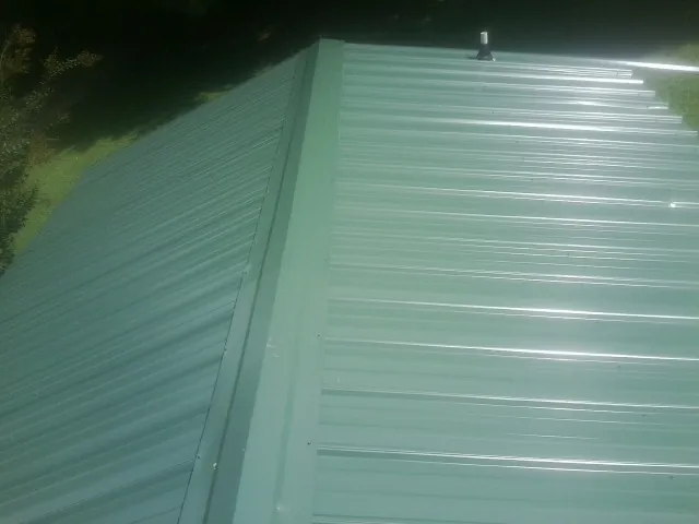 New green metal panels meeting at the ridge of a roof — Flat Roof Repair work by our crew in Carmine