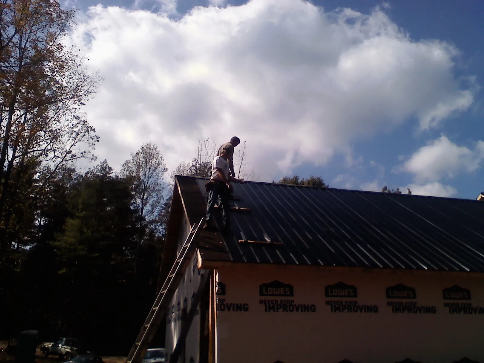 Roofer fastening dark metal panels high against a cloudy sky, from a Roof Inspection job in Carmine