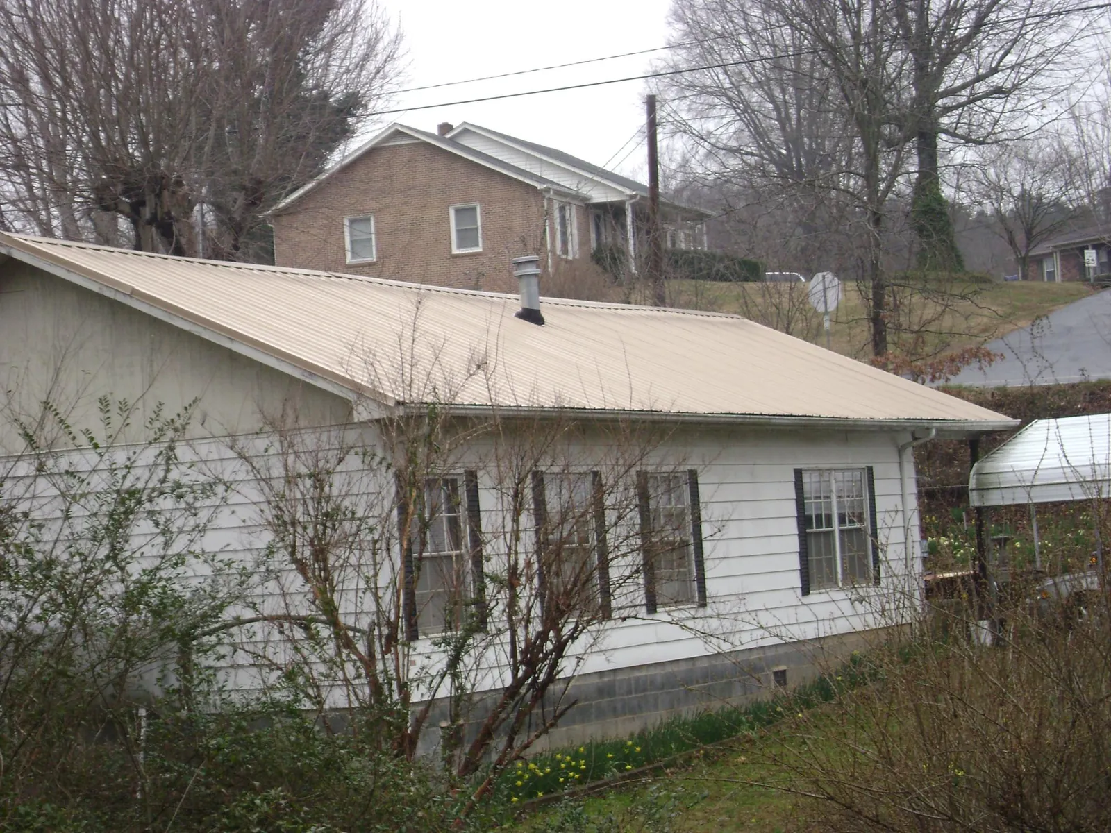 Tan metal roof on a white sided house set into a hillside — Commercial Roofing by Roofing Brothers in Carmine