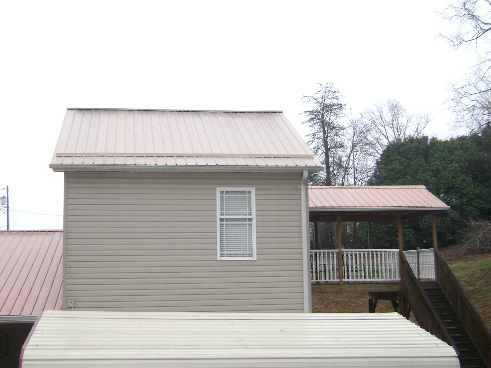 Tan metal roofs on a two story addition and attached porch, from a Roof Replacement job in Carmine